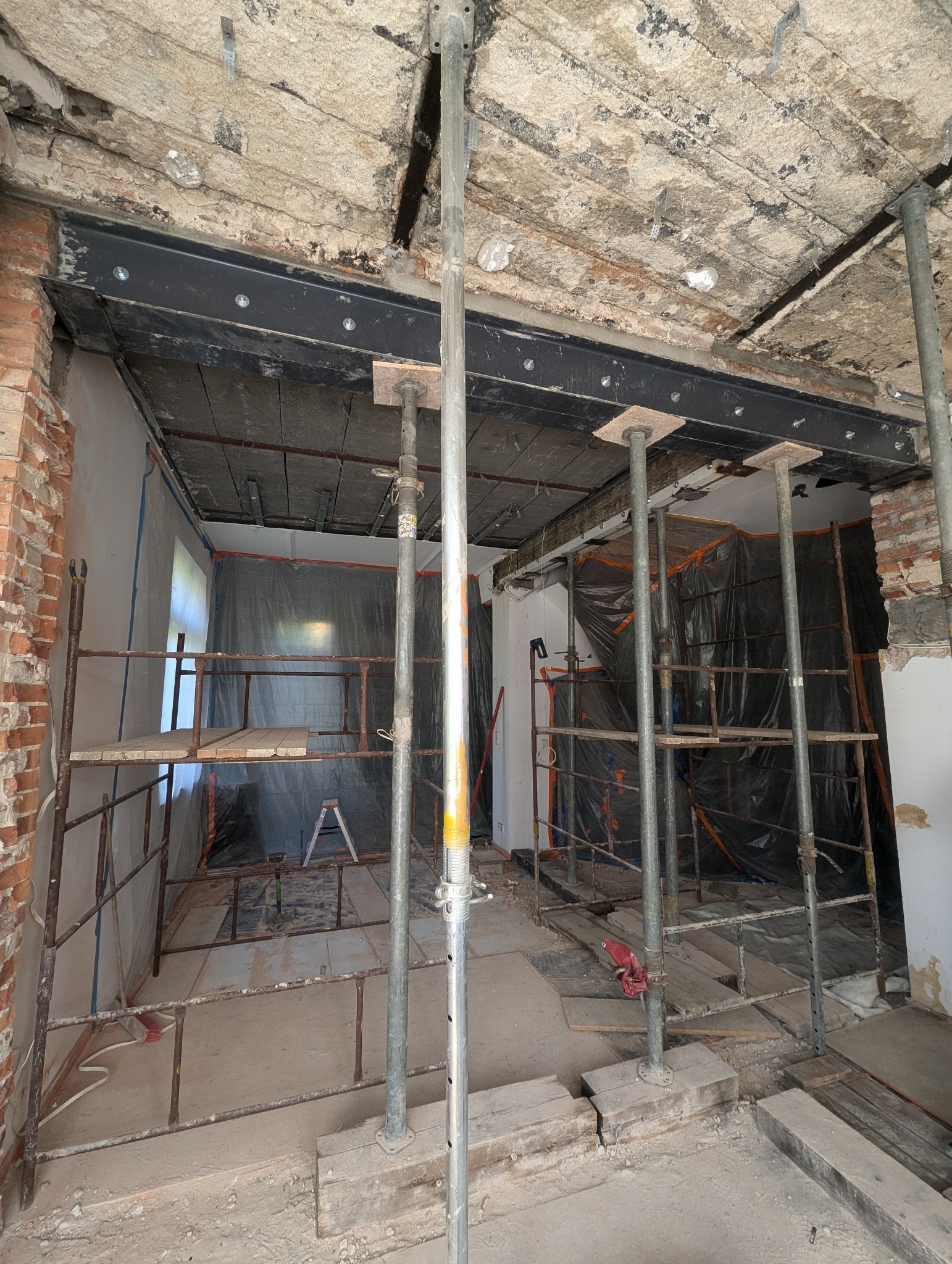 Wnętrze w trakcie remontu z podpartym stropem belkami stalowymi, widoczne rusztowania i zabezpieczenia folią.