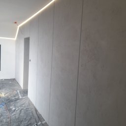 MiniBud remonty i wykończenia Roman Havryliuk - Ściana wykończona szarą, strukturalną farbą z oświetleniem LED wzdłuż sufitu, zabezpieczona folią podłoga w trakcie prac.