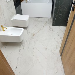 MiniBud remonty i wykończenia Roman Havryliuk - Nowoczesna łazienka z białą armaturą, złotą baterią i czarnymi płytkami imitującymi marmur na ścianach, jasne płytki podłogowe z marmurkowym wzorem, widok na wannę, toaletę i bidet.