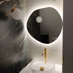 MiniBud remonty i wykończenia Roman Havryliuk - Nowoczesna łazienka z umywalką kryształową na blacie, złotą armaturą i podświetlanym lustrem o nieregularnym kształcie, ściany wyłożone płytkami imitującymi marmur w dwóch odcieniach.