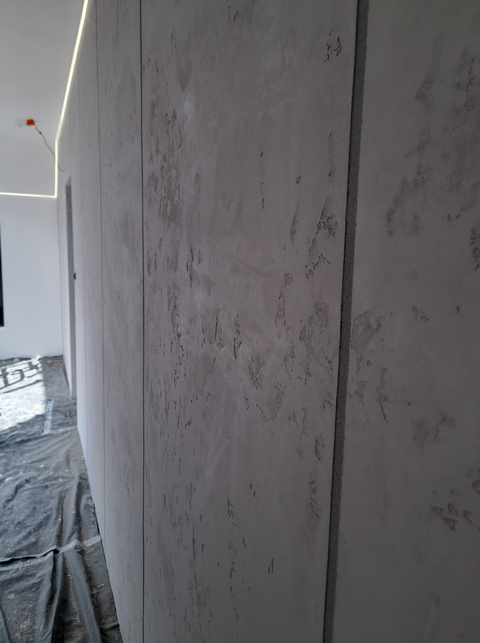 Ściana wykończona płytami kartonowo-gipsowymi z efektem dekoracyjnym w Katowicach, widoczne łączenia płyt i oświetlenie LED przy suficie, podłoga zabezpieczona folią.