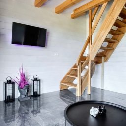 GRUCH - FACH Kewin Pałys - Jasne drewniane schody w nowoczesnym wnętrzu z białymi ścianami, widocznymi belkami stropowymi, szarą marmurową podłogą i czarnym stolikiem kawowym z dekoracjami.