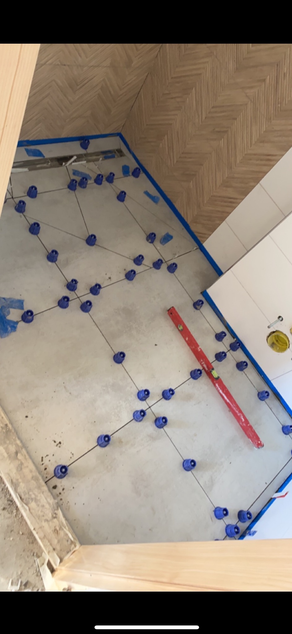 Widok z góry na przygotowany betonowy podkład podłogowy z systemem poziomowania płytek, poziomica na podłodze, ściana wykończona płytkami w jodełkę