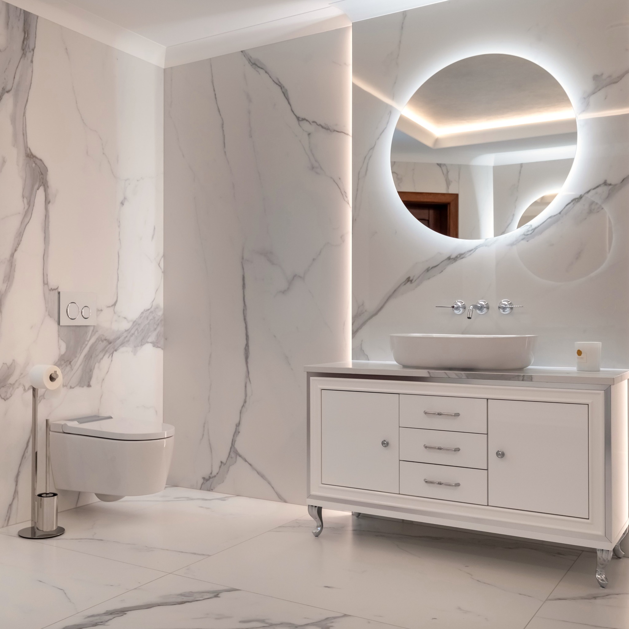 Elegancka łazienka z marmurowymi ścianami i podłogą, okrągłym lustrem z podświetleniem LED, wiszącą toaletą i białą szafką z umywalką.