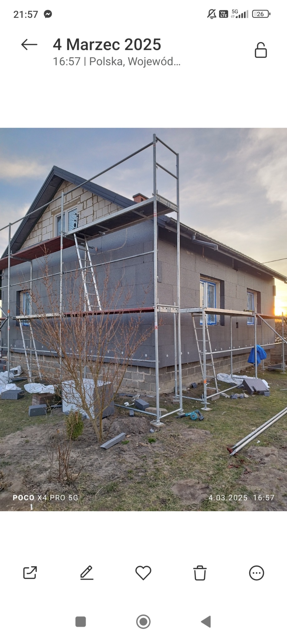 Dom jednorodzinny w trakcie ocieplania elewacji zewnętrznej, widoczne rusztowania, częściowo ocieplone ściany szarym styropianem, oraz odsłonięta cegła na górnej części ściany szczytowej