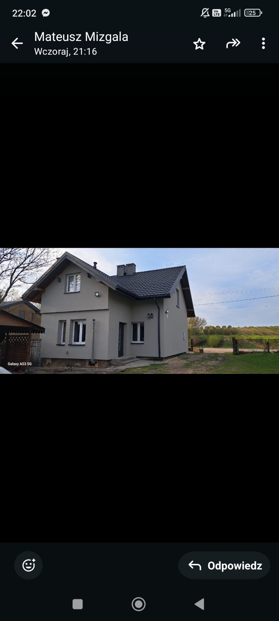 Ocieplony dom jednorodzinny z szarą elewacją i ciemnym dachem, widok z zewnątrz na tle zieleni.