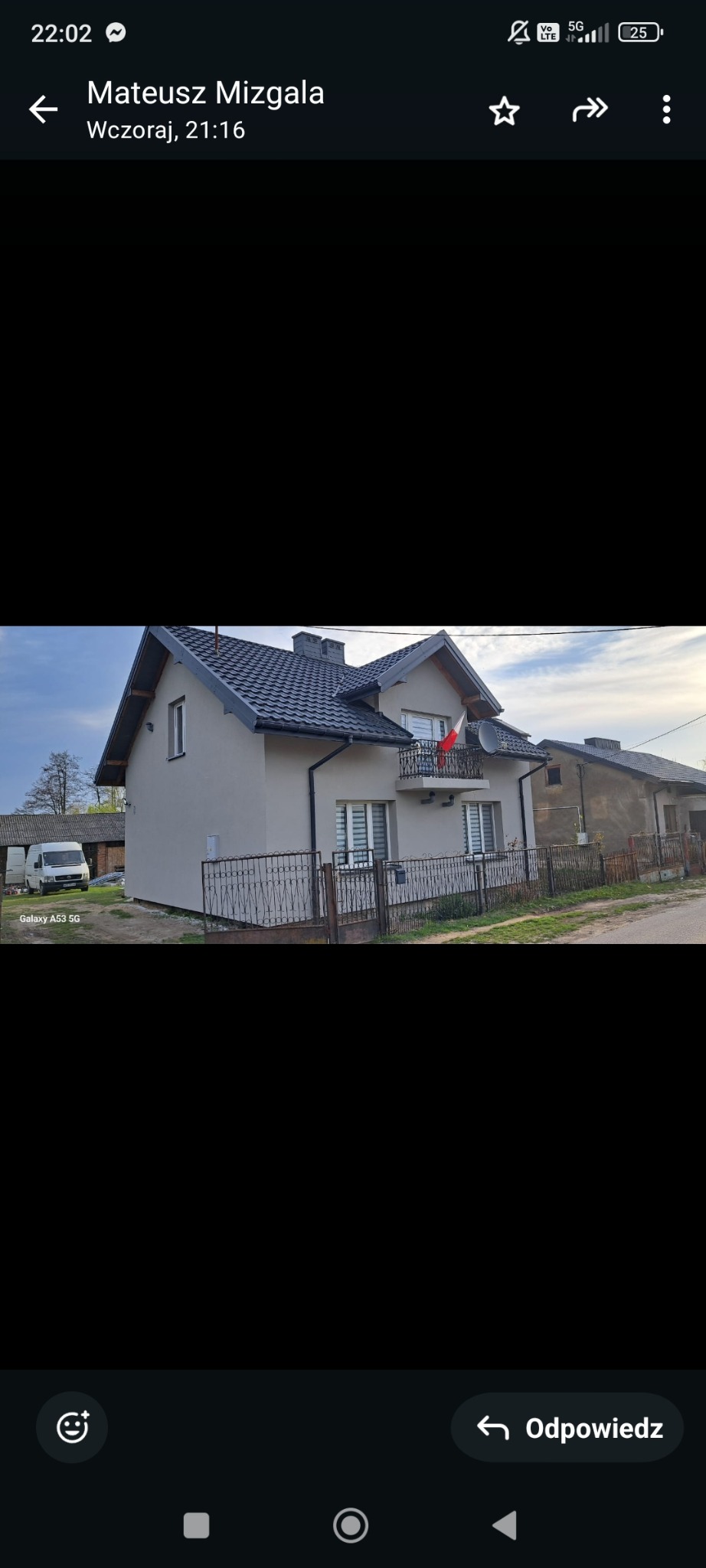 Jasnoszary dom jednorodzinny z ciemną dachówką i flagą Polski na balkonie, widoczny z zewnątrz, z samochodem dostawczym w tle.