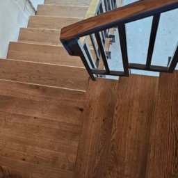 Holleywood - Drewniane schody z metalową balustradą, widok z góry, ukazujący strukturę drewna i detale wykończenia.