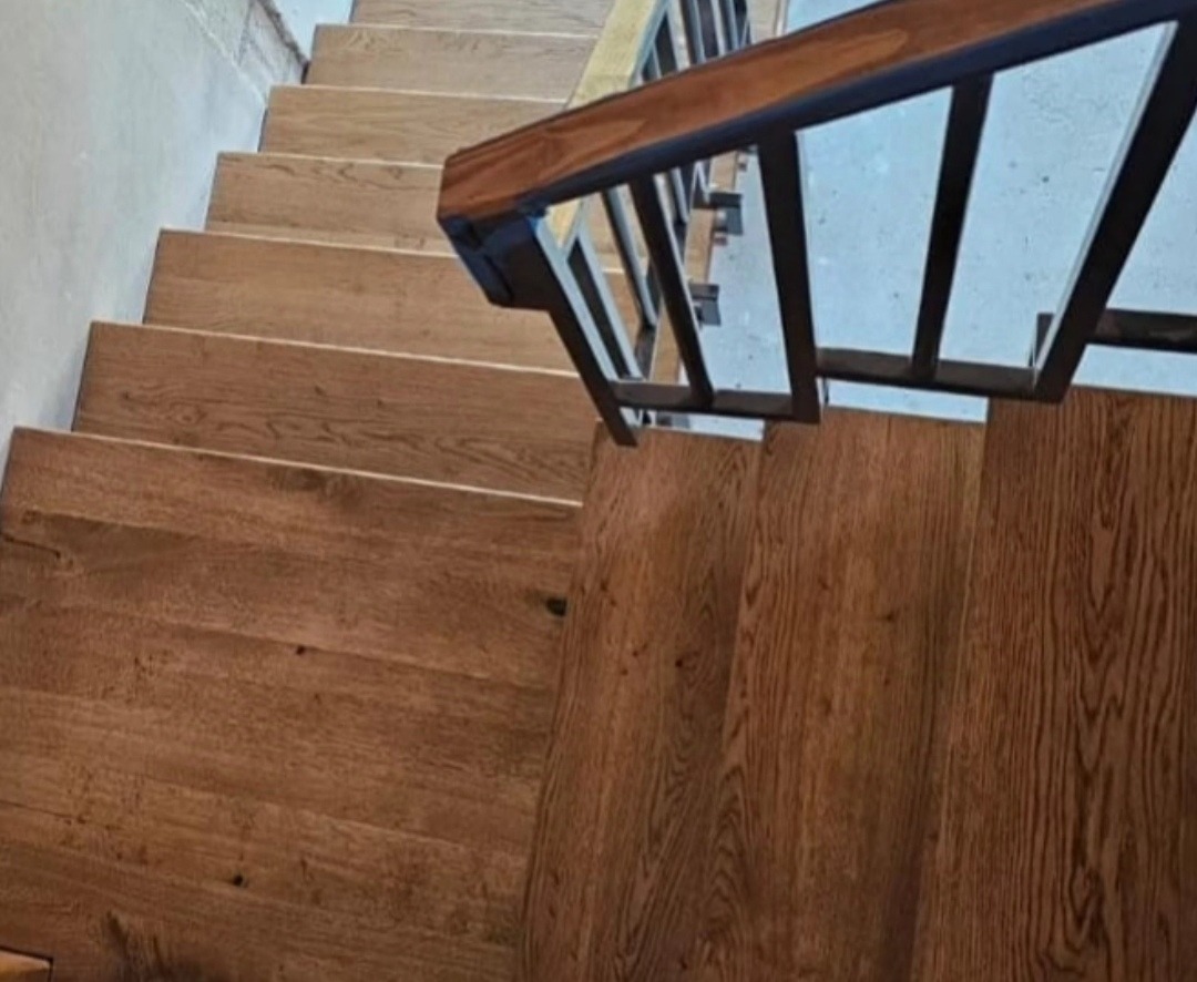 Drewniane schody z metalową balustradą, widok z góry, ukazujący strukturę drewna i detale wykończenia.