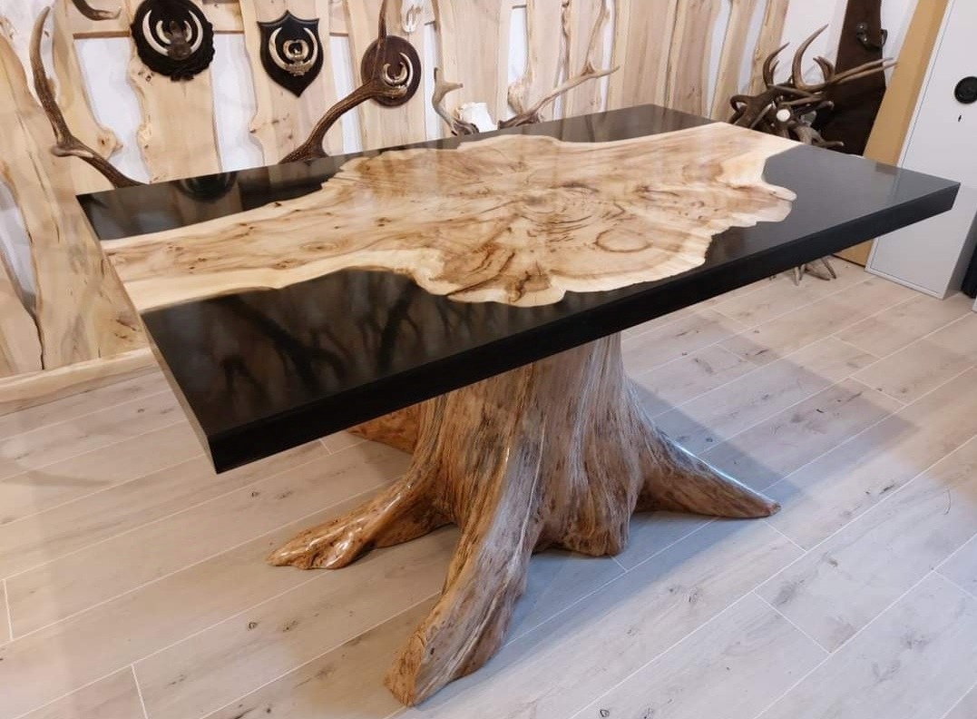 Stół z blatem z drewna i żywicy epoksydowej na podstawie z pnia drzewa, w tle ściana dekorowana trofeami myśliwskimi.