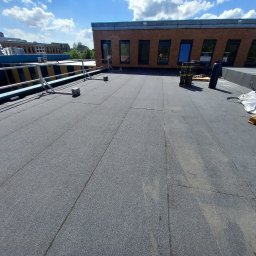 Dachwid - Wykończony, płaski dach pokryty papą termozgrzewalną na budynku w Sobkowie, widoczne zabezpieczenia krawędzi dachu i materiały budowlane na paletach.