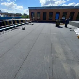 Wykończony, płaski dach pokryty papą termozgrzewalną na budynku w Sobkowie, widoczne zabezpieczenia krawędzi dachu i materiały budowlane na paletach.