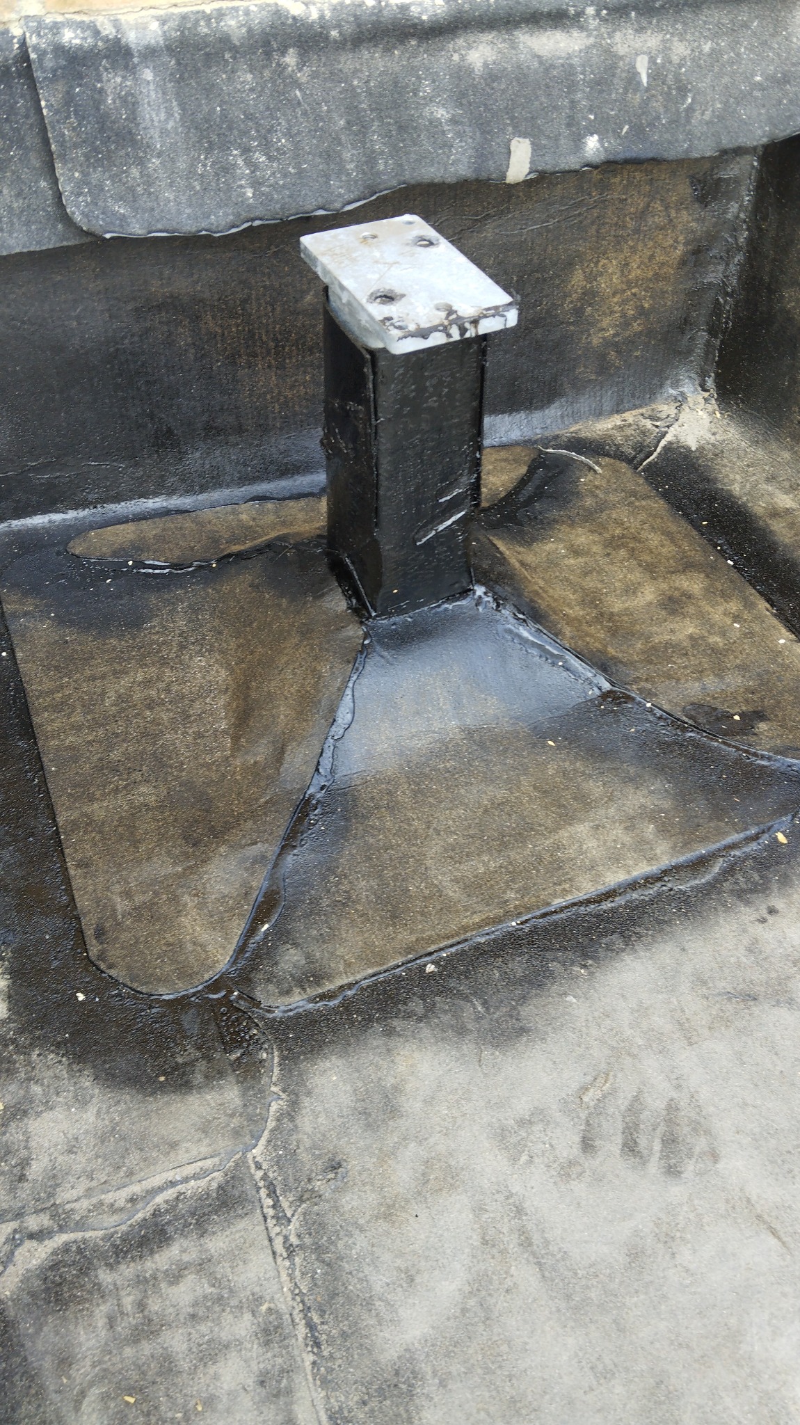 Szczegółowe ujęcie fragmentu płaskiego dachu po uszczelnieniu wokół metalowego wspornika w Sobkowie, widoczne ślady świeżego bitumu.