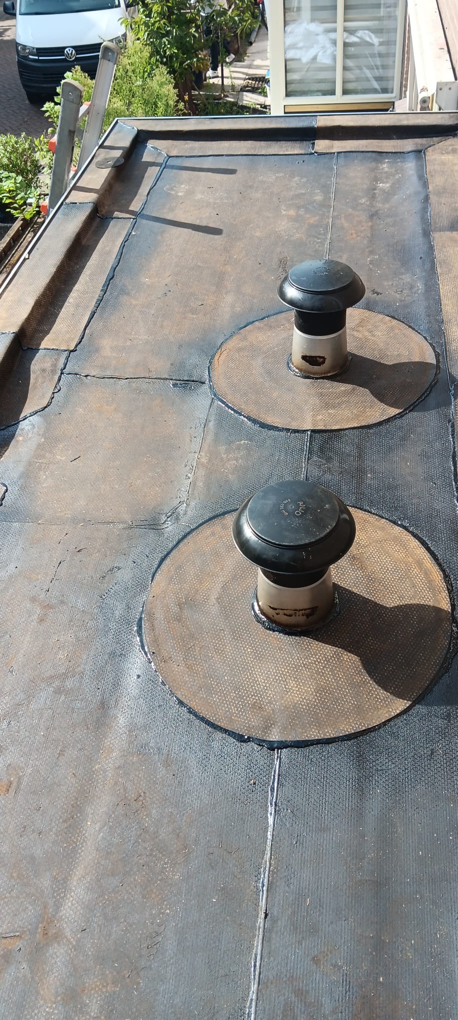 Płaski dach pokryty papą z dwoma kominkami wentylacyjnymi, widoczne łączenia papy i obróbki blacharskie przy krawędzi dachu.