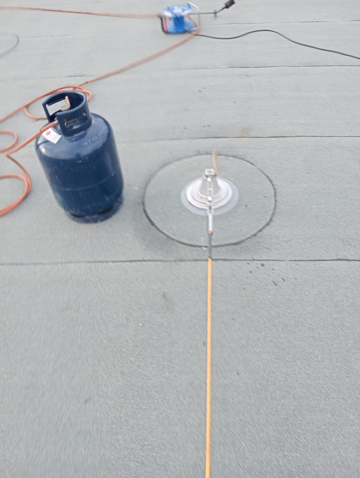 Butla gazowa i narzędzia na płaskim, szarym dachu z papy, widoczna linia wyznaczająca kierunek obróbki detalu.