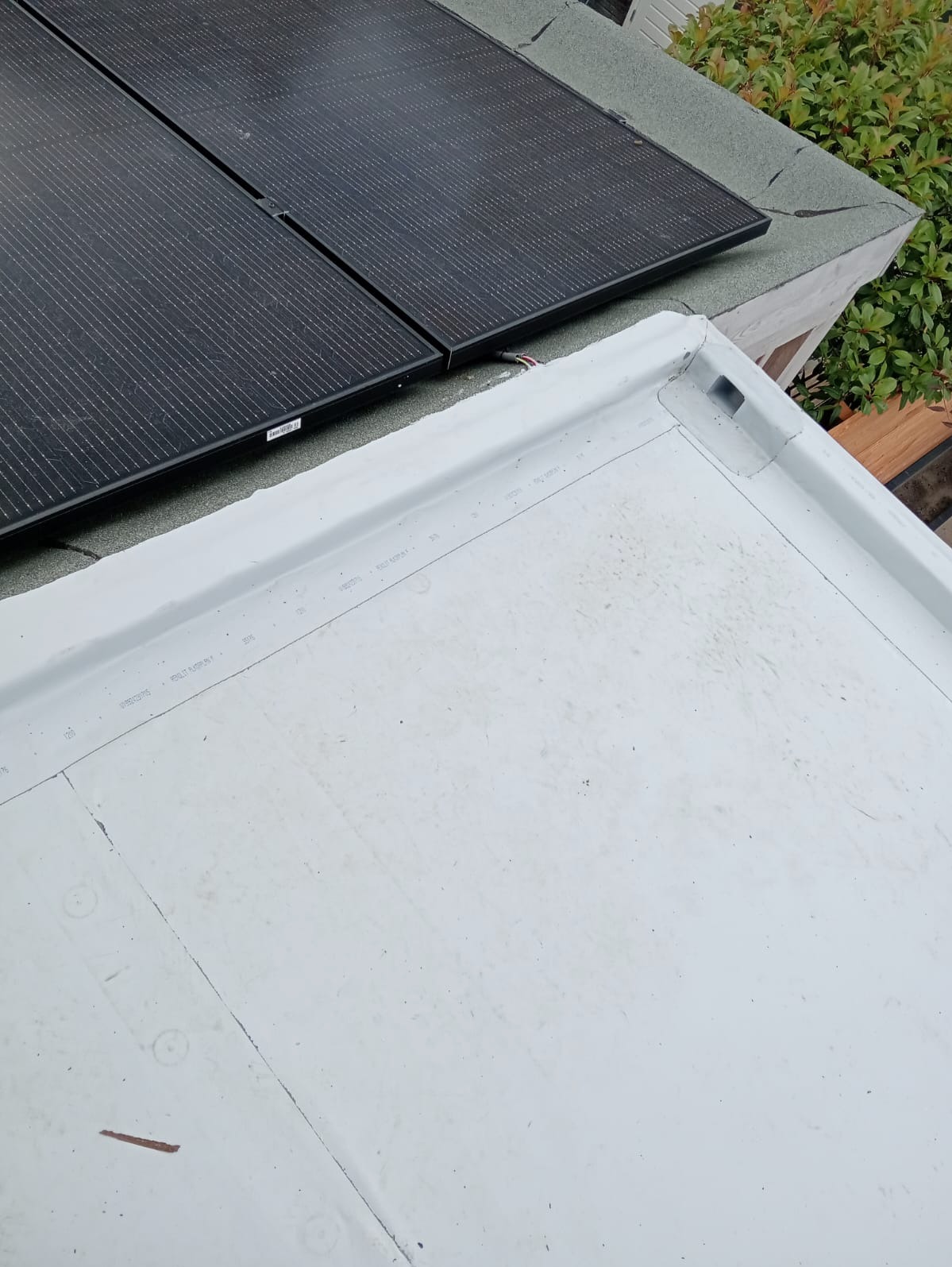 Biała, płaska powierzchnia dachu z widocznymi panelami słonecznymi w górnym rogu i elementami wykończeniowymi przy krawędziach.