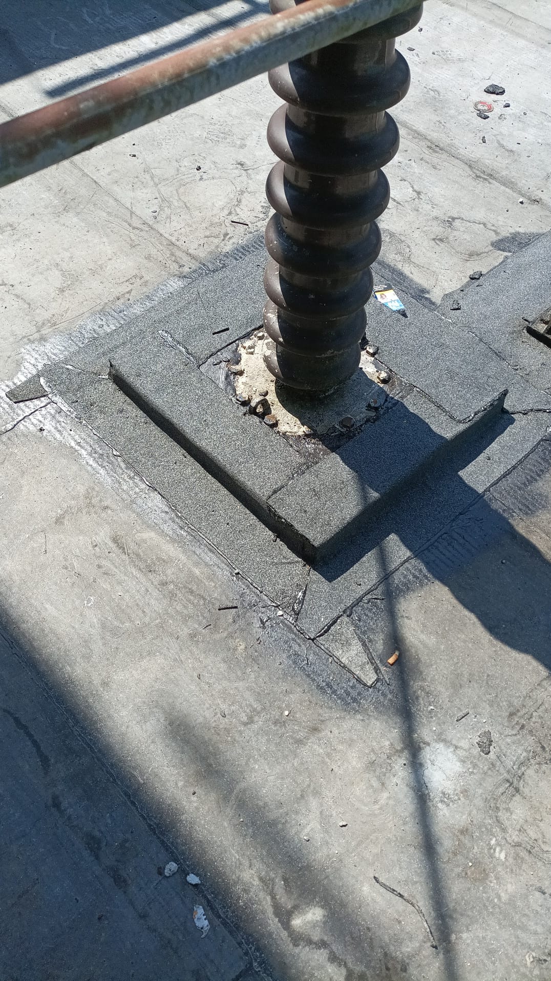 Szczegółowe ujęcie izolacji wokół pionowego elementu na płaskim dachu pokrytym papą, z widocznymi obróbkami blacharskimi i uszczelnieniami.