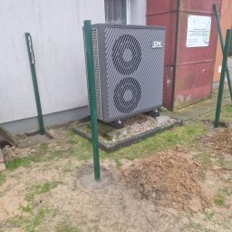 KWS - Przygotowania do montażu ogrodzenia: wbite słupki w ziemię obok ułożonej kostki brukowej pod pompę ciepła Cooper&Hunter, sterta kostki z boku.