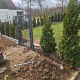 KWS - Montaż ogrodzenia panelowego z siatki w trakcie prac ziemnych, widoczna brama, narzędzia, sadzonki tui i dostawczy samochód w tle.