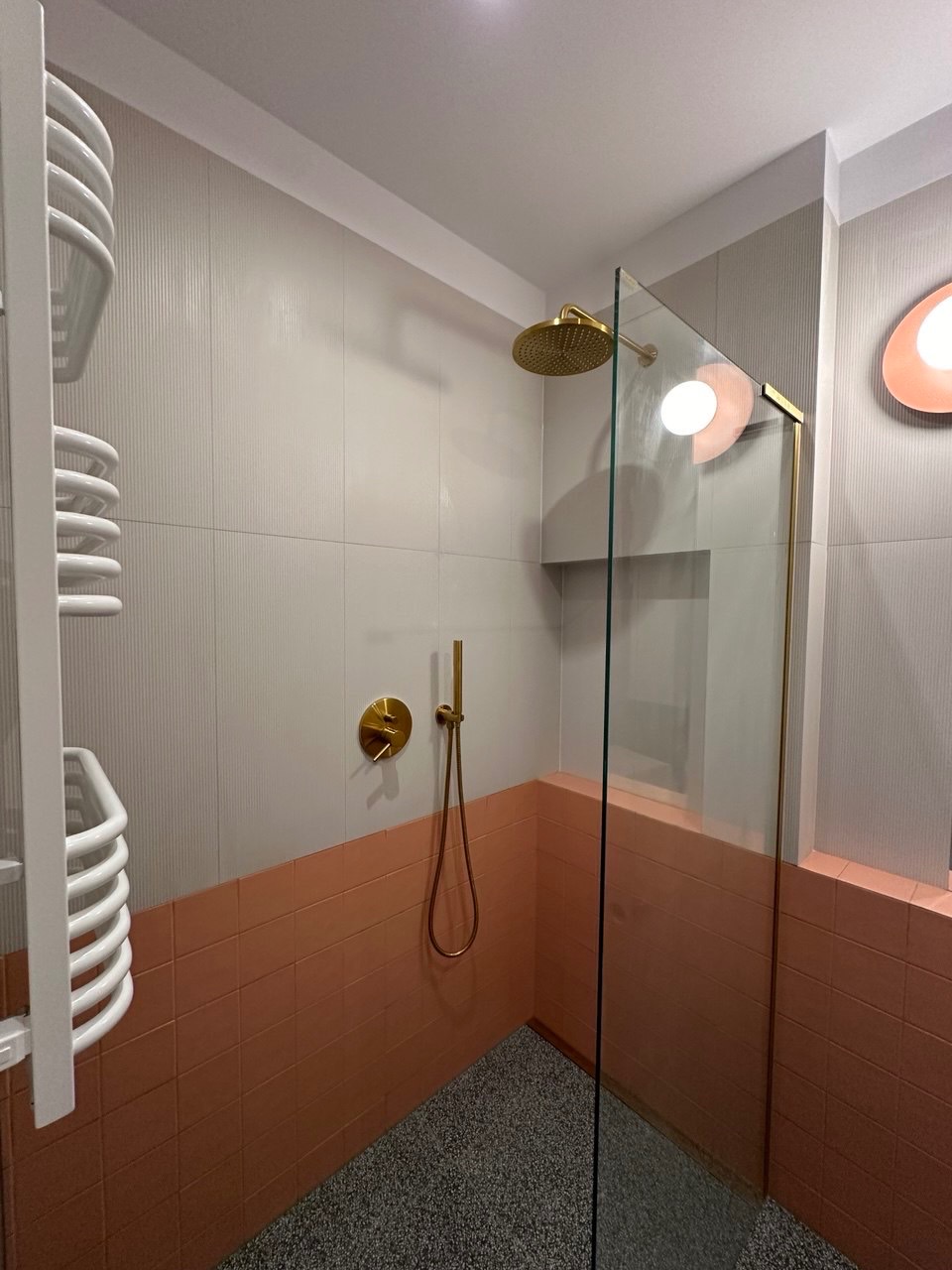 Nowoczesna kabina prysznicowa z elementami w kolorze złota, jasnymi płytkami i grzejnikiem drabinkowym.