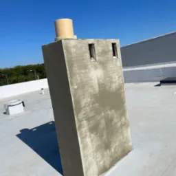 Wymurowany komin na dachu budynku przemysłowego, z widocznymi otworami wentylacyjnymi i elementami izolacji, w trakcie prac wykończeniowych.