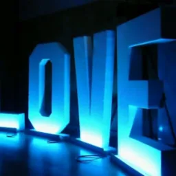 Duże, białe, podświetlane na niebiesko litery tworzące słowo LOVE stojące na podłodze w ciemnym otoczeniu.
