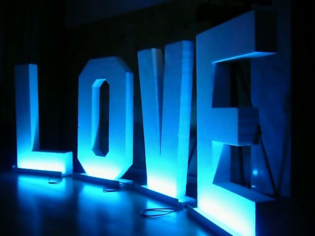 Duże, białe, podświetlane na niebiesko litery tworzące słowo LOVE stojące na podłodze w ciemnym otoczeniu.