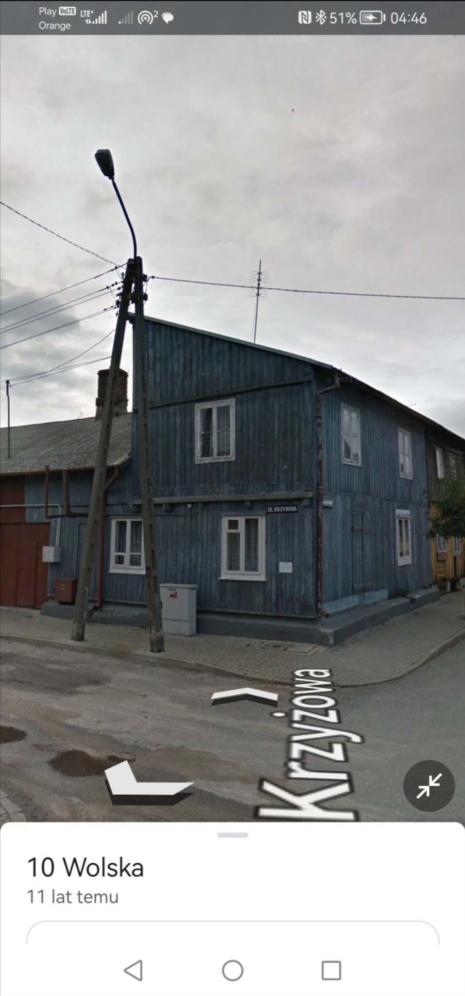 Dwukondygnacyjny, niebieski, drewniany dom z białymi oknami, widziany z poziomu ulicy Krzyżowej, z słupem elektrycznym na pierwszym planie.