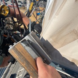 Usługi alpinistyczne Oskar Foitzik - Pracownik w uprzęży, z bliska trzymający narzędzie do czyszczenia pionowej powierzchni, prawdopodobnie elewacji budynku. W tle widoczny port lotniczy z samolotami.