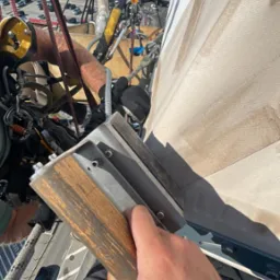 Pracownik w uprzęży, z bliska trzymający narzędzie do czyszczenia pionowej powierzchni, prawdopodobnie elewacji budynku. W tle widoczny port lotniczy z samolotami.