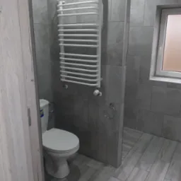 Wykończona łazienka w szarościach: płytki imitujące drewno na podłodze i ścianach, biała toaleta i grzejnik drabinkowy, widok zza uchylonych drzwi.