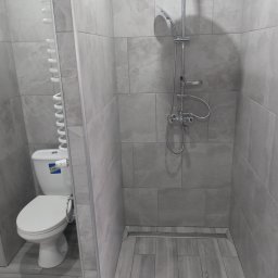 Bolesław - Wykończona łazienka w odcieniach szarości, z kabiną prysznicową typu walk-in, odpływem liniowym w podłodze wyłożonej płytkami imitującymi drewno oraz toaletą z grzejnikiem drabinkowym.