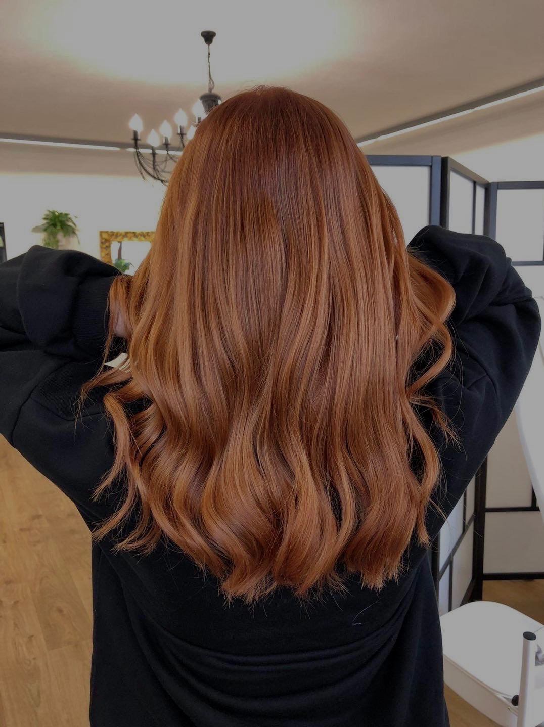 Długie, miedziane włosy z delikatnymi falami, widok z tyłu, osoba w czarnej bluzie trzyma ręce za głową.