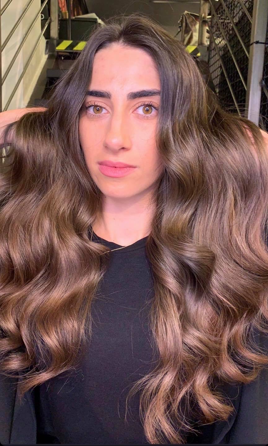 Portret kobiety z długimi, brązowymi włosami z delikatnymi falami i subtelnym ombre, modelka patrzy prosto w obiektyw, prezentując efekt stylizacji w salonie.