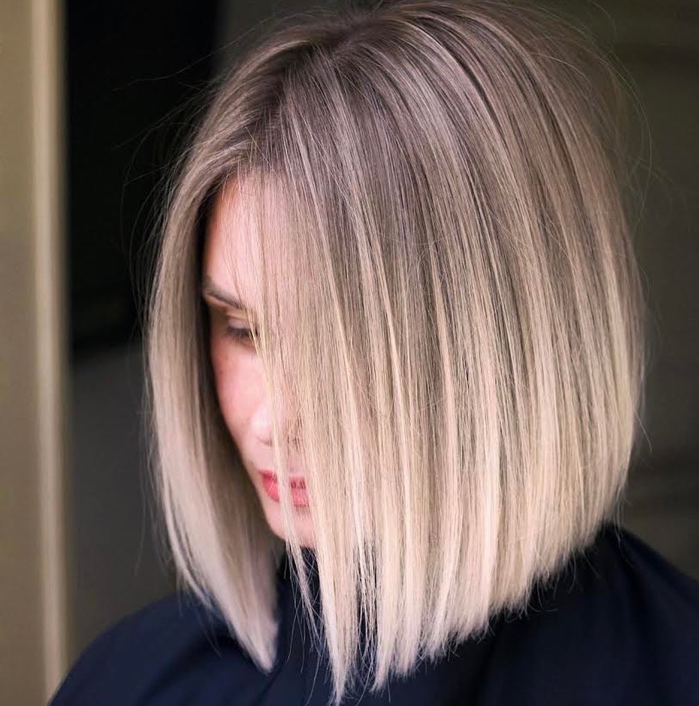 Krótkie, proste, blond włosy z ciemniejszym odrostem, częściowo zakrywające twarz, z delikatnym makijażem.