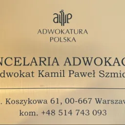 Złota tabliczka informacyjna z napisem 'Kancelaria Adwokacka Adwokat Kamil Paweł Szmidt', adres ul. Koszykowa 61 w Warszawie i numer telefonu.