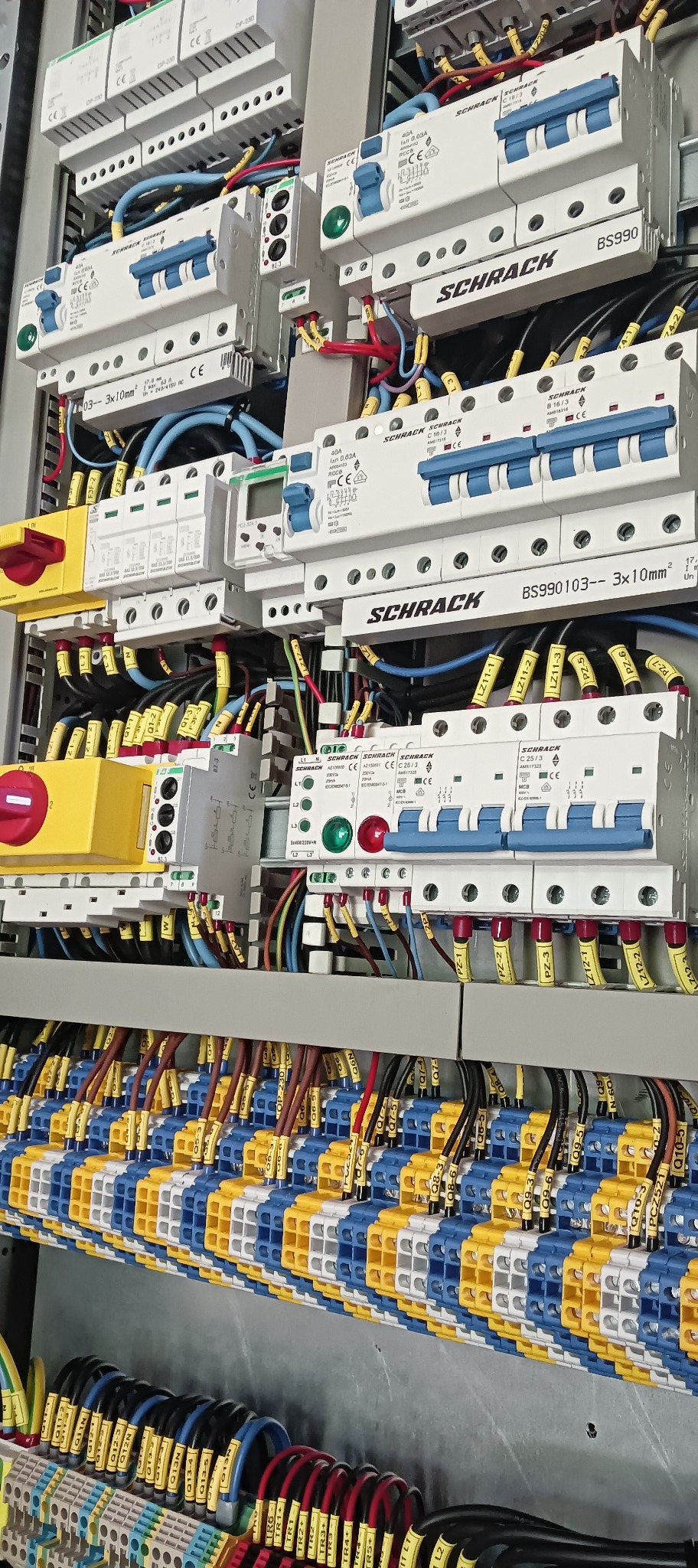 Rozbudowana rozdzielnica elektryczna z licznymi zabezpieczeniami, przewodami oznaczonymi opisami, widoczne bezpieczniki i wyłączniki różnicowoprądowe marki Schrack, ułożone w uporządkowany sposób.