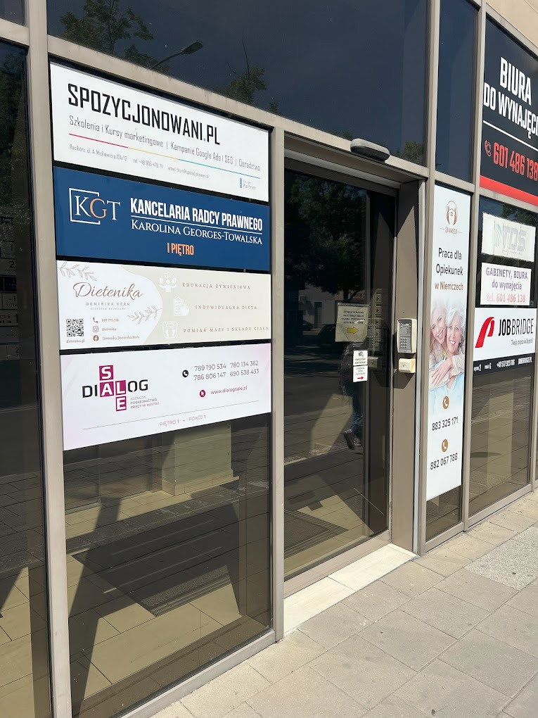 Tablica informacyjna na elewacji budynku z ogłoszeniami różnych firm, w tym gabinetu oferującego edukację żywieniową i indywidualne diety. Widoczne logo i dane kontaktowe.