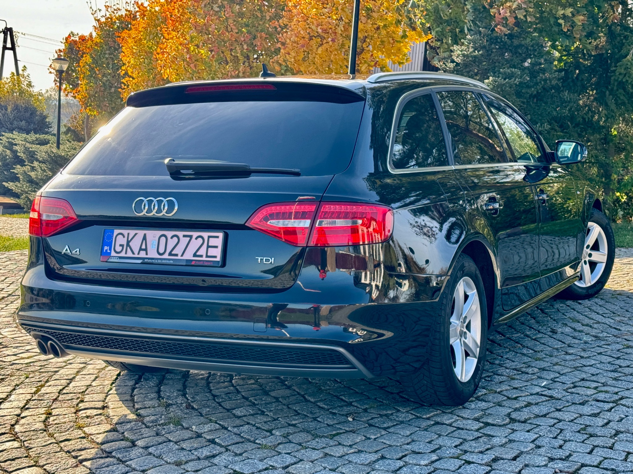 Czarny samochód Audi A4 Avant TDI zaparkowany na brukowanej nawierzchni, widok z tyłu, jesienne drzewa w tle.