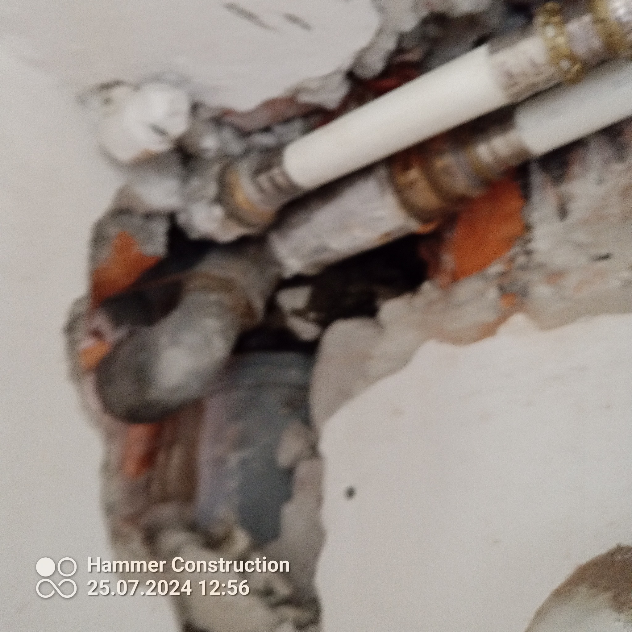 Fragment instalacji wodnej z rurami PEX i mosiężnymi złączkami, osadzony w ścianie z widocznymi śladami po kuciu i zaprawie.