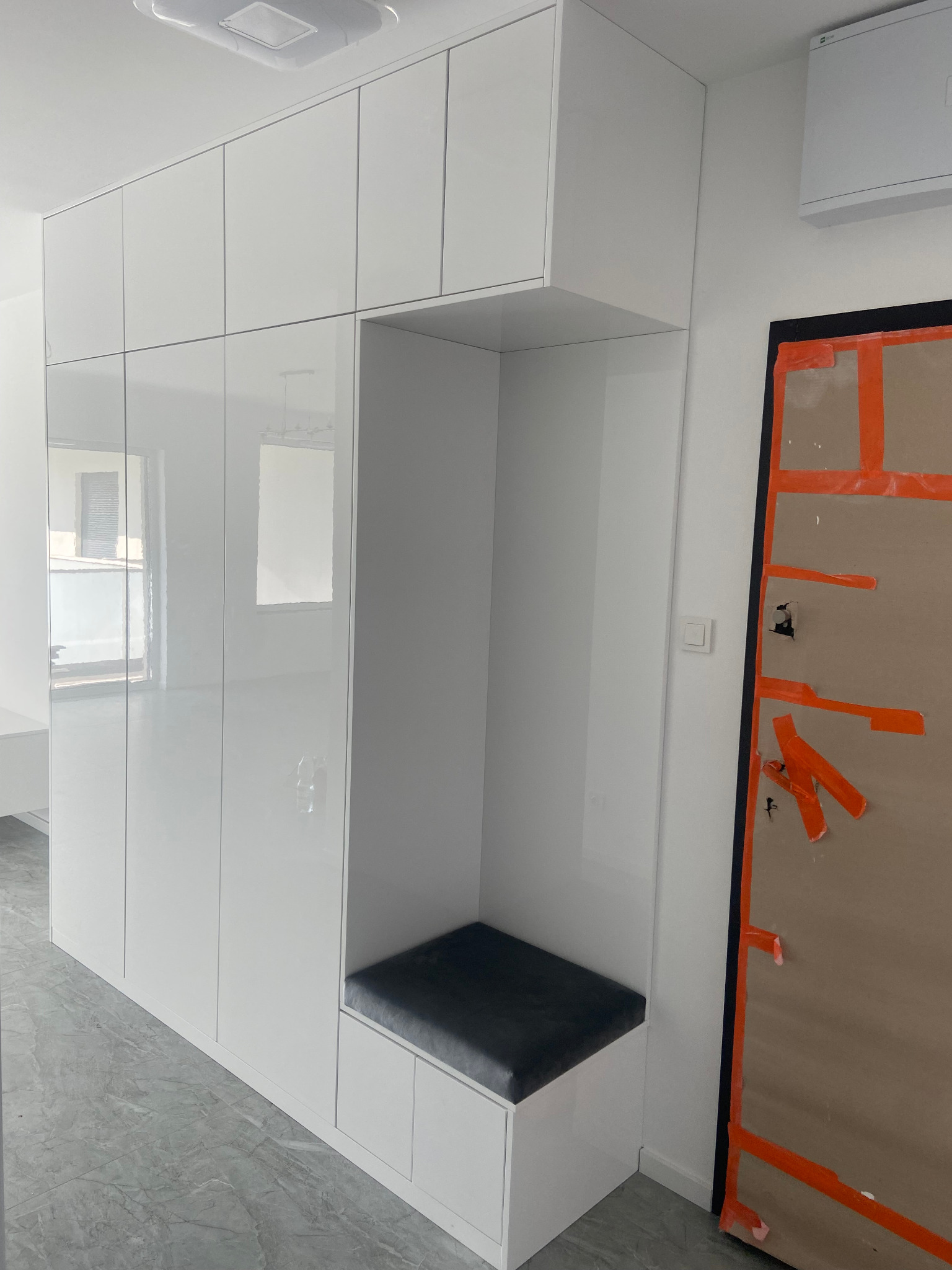 Biała szafa wnękowa z siedziskiem w przedpokoju, drzwi zabezpieczone taśmą malarską.