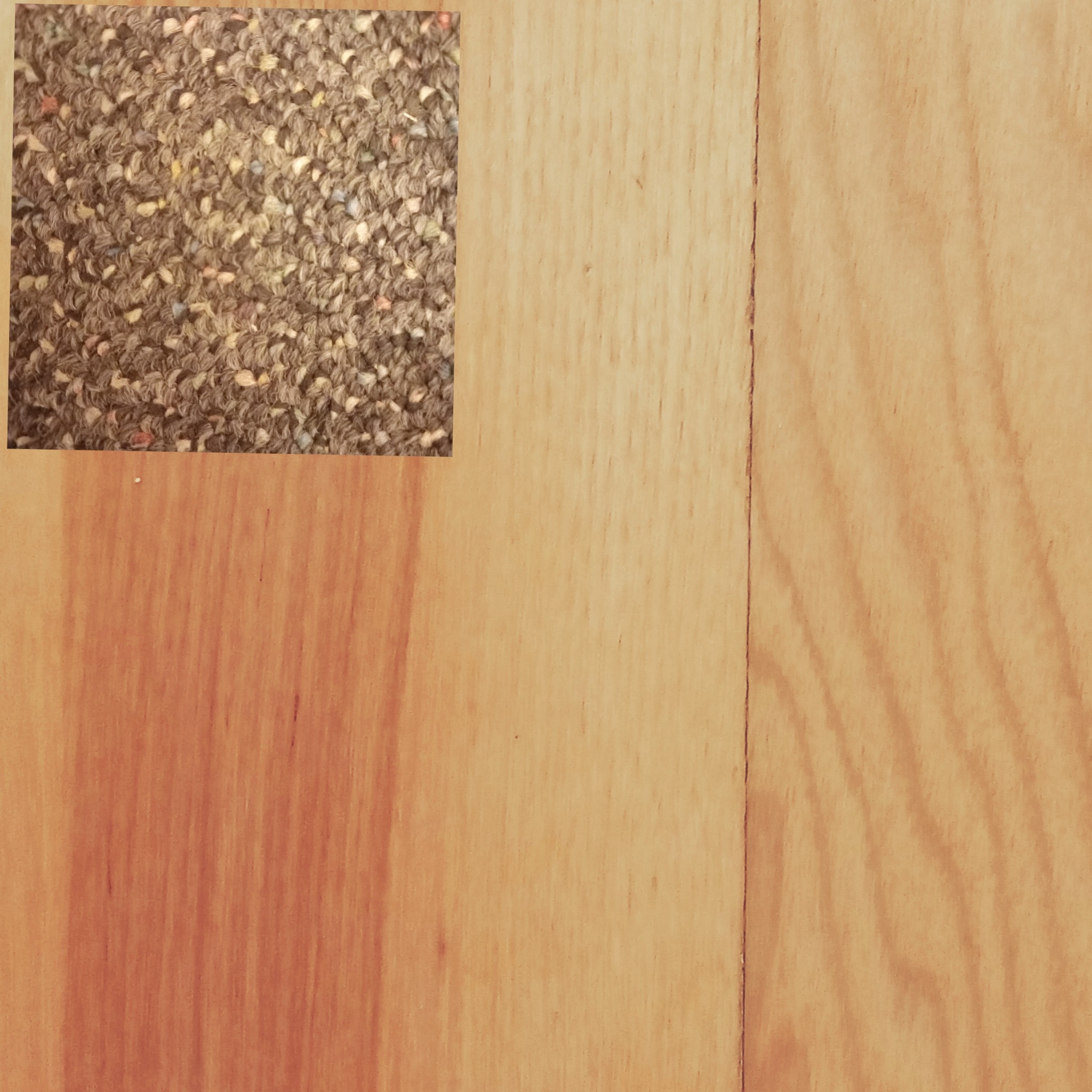 Fragment brązowej wykładziny dywanowej z kolorowymi włóknami, umieszczony na drewnianej podłodze z widocznymi słojami.