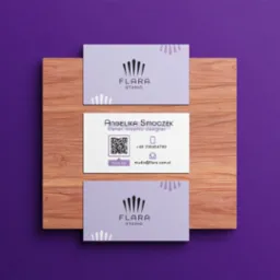 Trzy wizytówki firmy Flara Studio na drewnianej desce, fioletowe tło, minimalistyczny design, widoczny kod QR i dane kontaktowe.