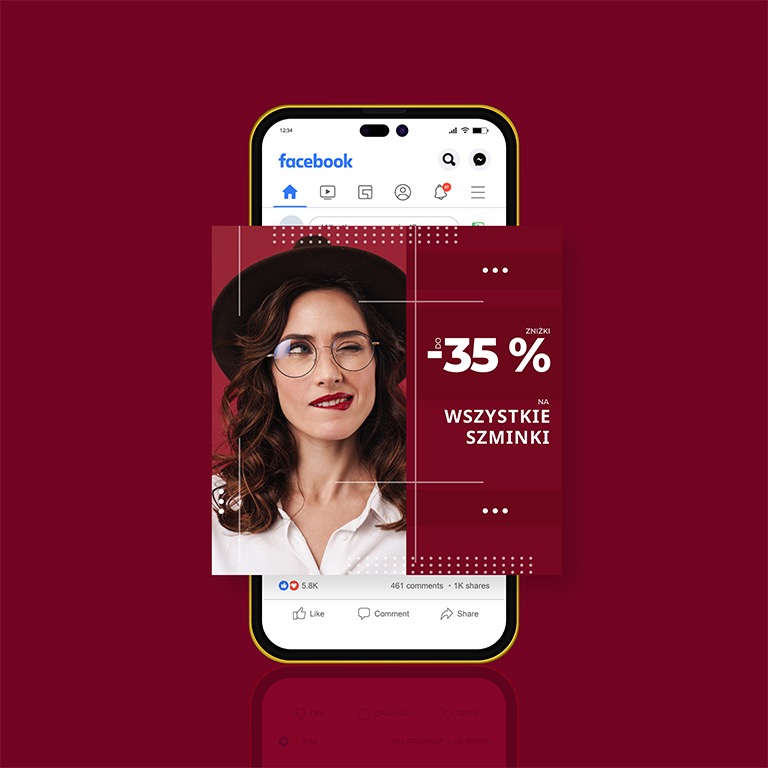 Smartfon wyświetlający reklamę na Facebooku z wizerunkiem kobiety w kapeluszu i okularach, informującą o 35% zniżce na szminki, na burgundowym tle.