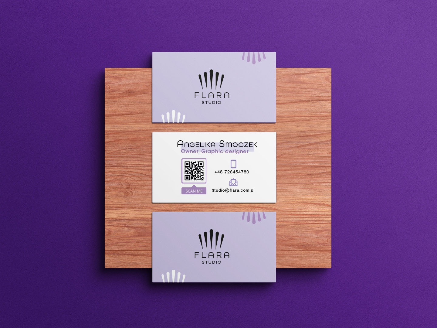 Trzy wizytówki firmy Flara Studio na drewnianej desce, fioletowe tło, minimalistyczny design, widoczny kod QR i dane kontaktowe.