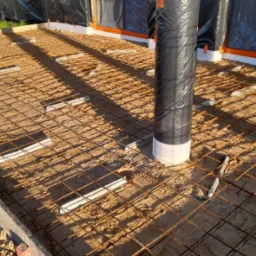 Przygotowanie podłoża pod wylewkę: siatka zbrojeniowa na podkładkach dystansowych, otuliny słupów zabezpieczone folią, widoczne szalunki obwodowe.