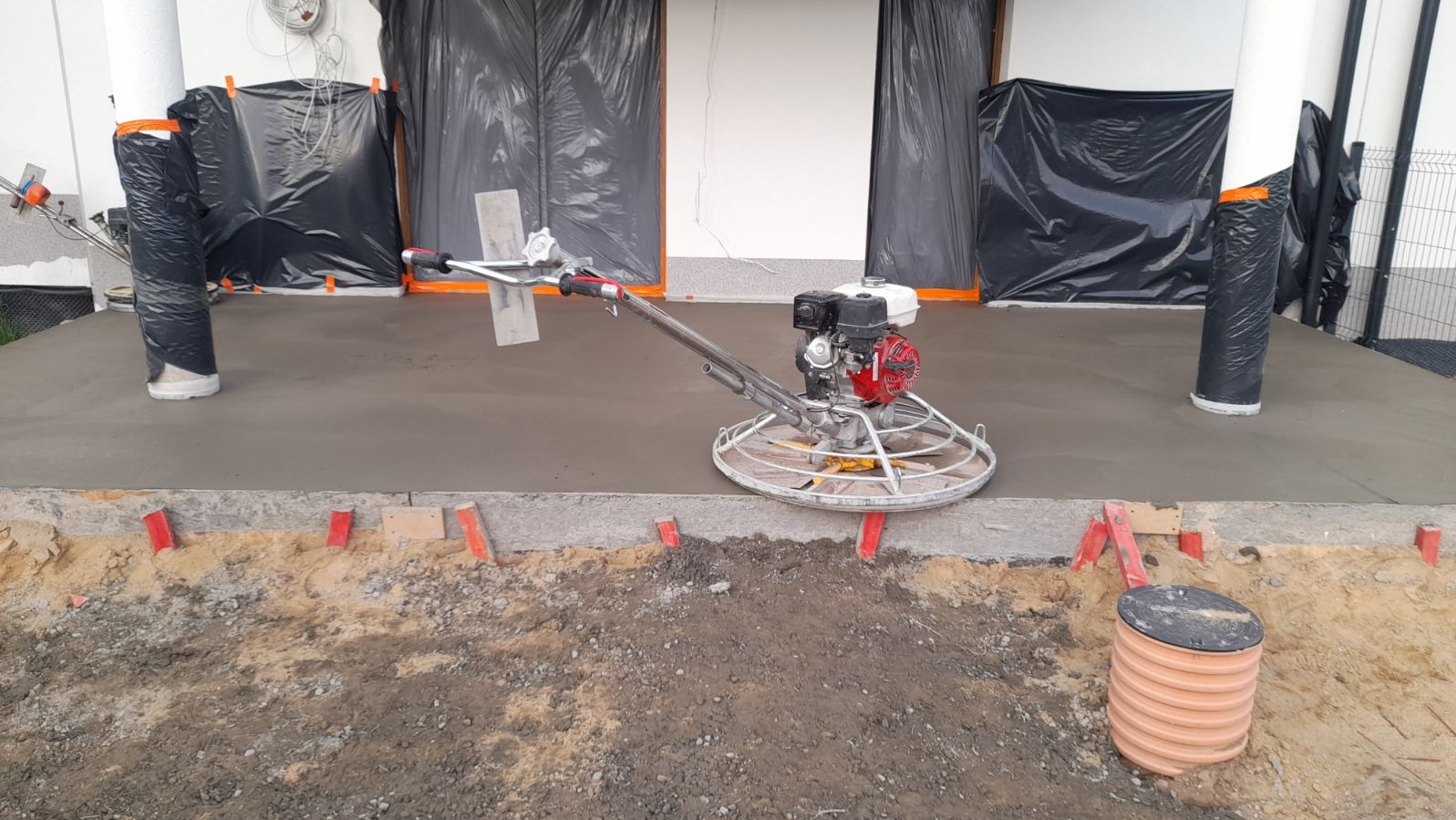 Zacieraczka mechaniczna do betonu na świeżo wylanej posadzce przemysłowej, z zabezpieczonymi folią kolumnami i ścianami.