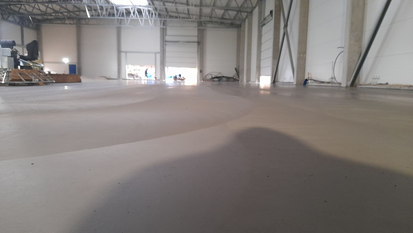 Świeżo wylana, gładka posadzka w hali przemysłowej w Strzelinie, z widocznym zarysem cienia na powierzchni.
