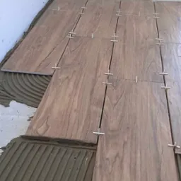 Proces układania płytek imitujących drewno na podłodze, widoczny klej i krzyżyki dystansowe.