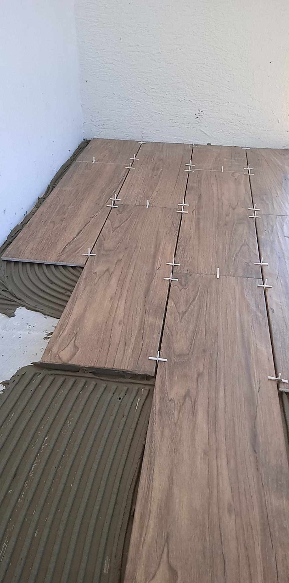 Proces układania płytek imitujących drewno na podłodze, widoczny klej i krzyżyki dystansowe.